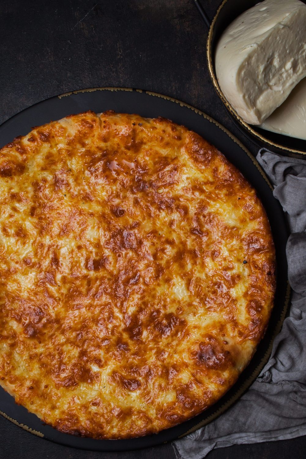 Top view khachapuri with sulguni cheese in dark plate on stone background